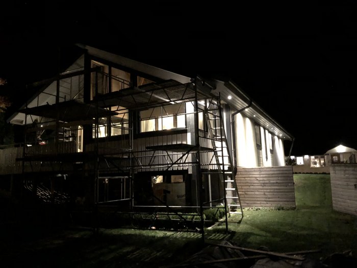 Hus under renovering på kvällen med upplyst fasad och byggställningar runtomkring.