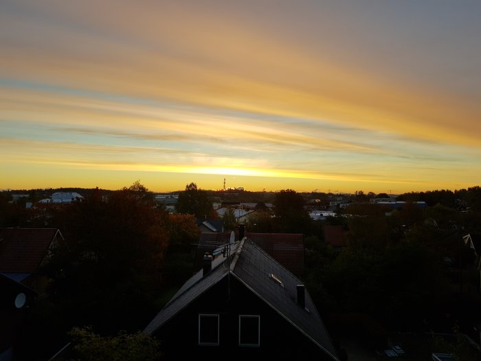 Soluppgång över ett bostadsområde med färgstark himmel och silhuetter av hus.