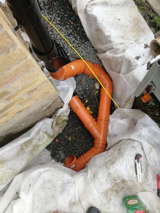 Nyinstallerade orangea dräneringsrör och dagvattenanslutning vid en byggnad.