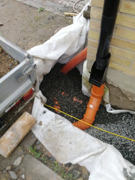 Nyinstallerat dräneringsrör och dagvattenanslutning vid husgrund med synligt rör för markränna.