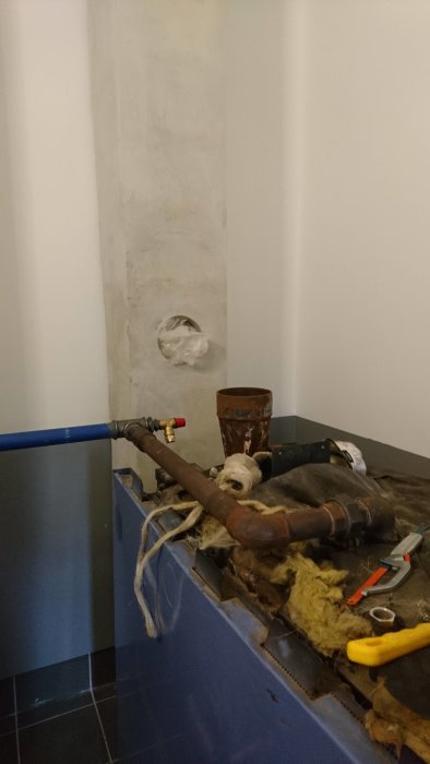 Renoveringsarbete med rörledningar och verktyg framför en betongvägg med ett hål.