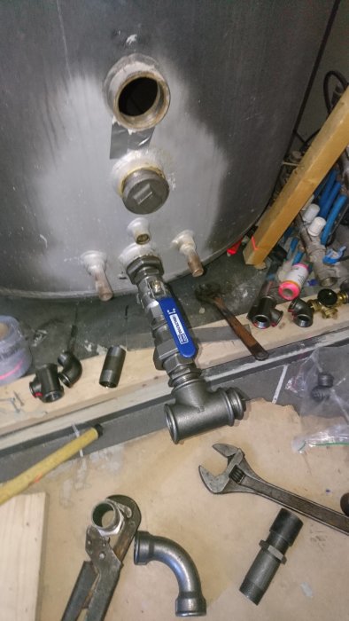 Installation av rör och ventiler nära en panna, verktyg och rördelar på golvet.