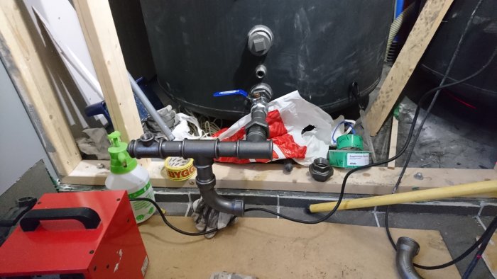 Rörsystem vid värmepanna under installation med verktyg och byggmaterial omkring.