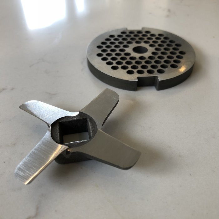 Slipdel och kvarnkniv i metall från en sliperifirma placeras på en marmorbänk.