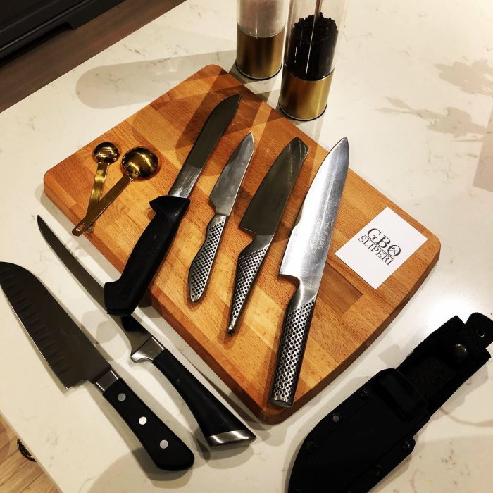 Olika typer av slipade knivar och saxar på en skärbräda märkt med "GBO Sliperi".