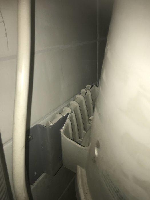 Vit dammsugare med en v-formad plåtbit delvis infäst vid en vit radiator, närbild på fästdetaljen.