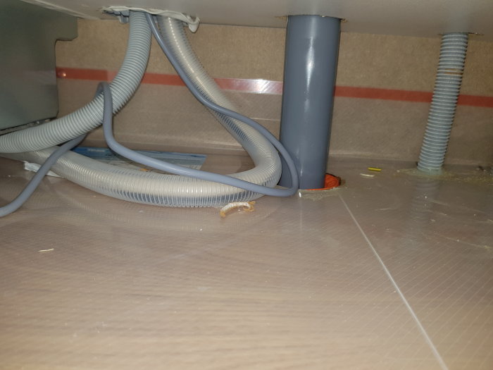 Installation under diskbänk med hål i droppskydd genom vilket rör och sladdar dragits.