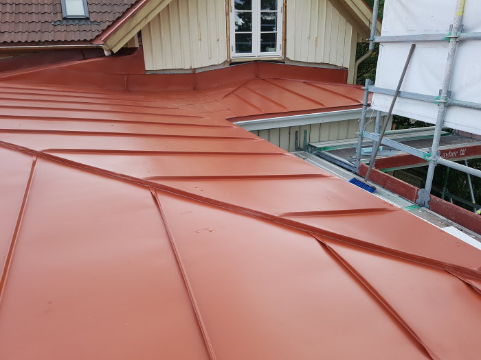 Rött pulpettak på byggnad utan nockventilation, med synlig ventilation mot fasaden och byggställning.