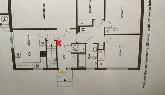 Planritning av hus med markerat förslag för luftvärmepumpens placering vid ett rött kryss.