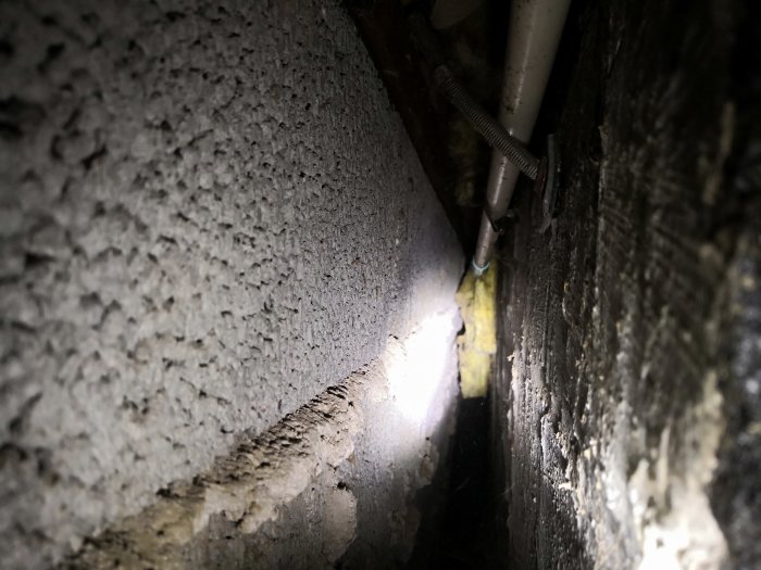 Glipa mellan källarväggarna i en plintgrund med synliga rör och isolering, tecken på mögliga problem med fukt och ventilation.