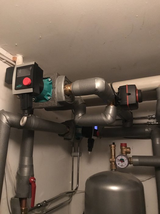 Komplex uppsättning av VVS-installationer med rör, ventiler och cirkulationspump i en pannrumsmiljö.