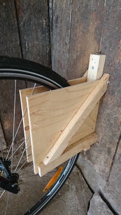 Hemmagjort träcykelställ fastskruvat på en trävägg med en cykeldäck vilar mot det.