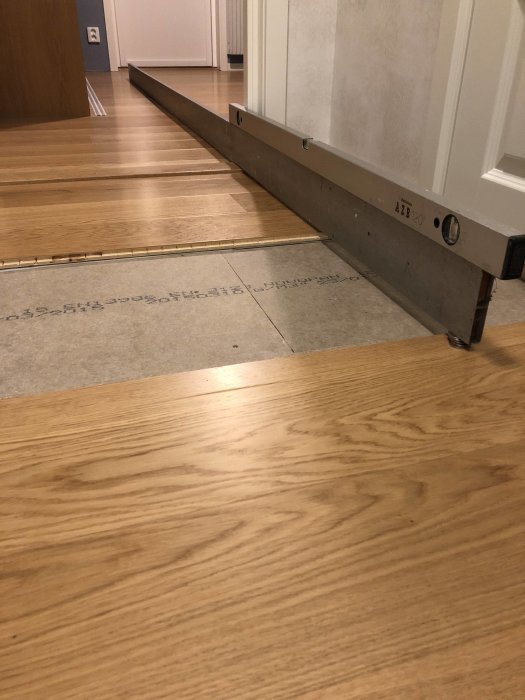 Lång nivellist som visar höjdskillnaden i ett golv med parkett och undergolv.