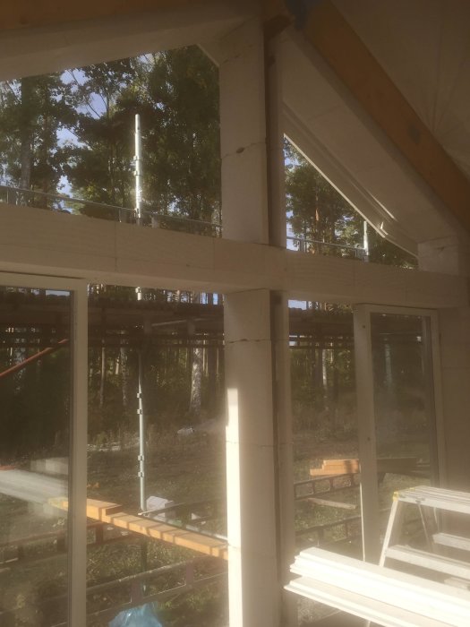 Inmurad järnpelare i en byggarbetsplats för stora fönster i ett hus under konstruktion, med skog i bakgrunden.