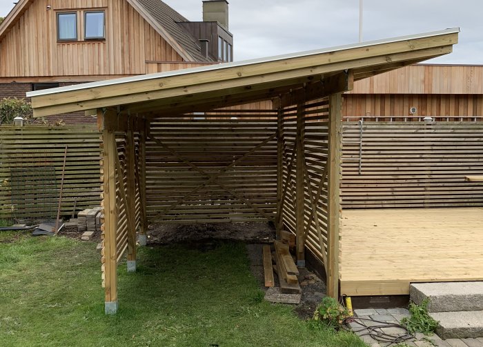 Nybyggd träpergola med kryssmönstrad ribbning, takpapp och skyddande plåt på toppen.