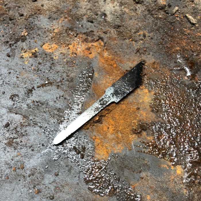 Handsmidd och slipad märkkniv av högkolhaltigt stål, härdad och glashård, på en rostig yta.