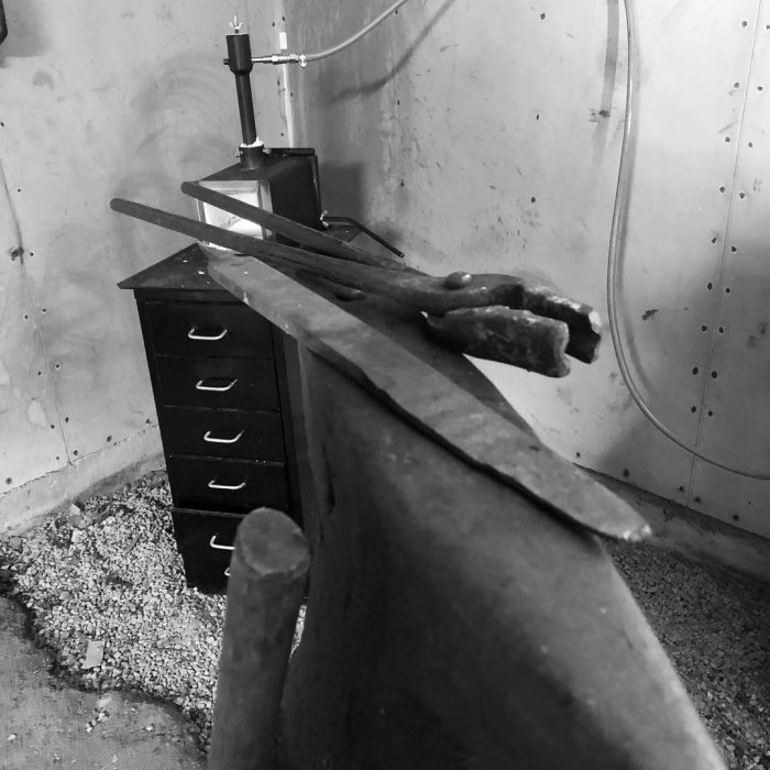 Hantillverkad märkkniv ligger på ambolten i en smedja, bredvid gamla filar och smidesutrustning.
