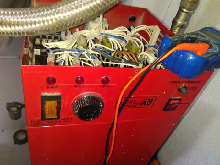 Öppen röd elpanna med synlig intern kabeldragning och termostat, några etiketter syns.