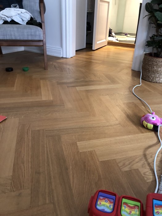 Ekparkett i fiskbensmönster i ett rum med leksaker och möbler syns delvis.