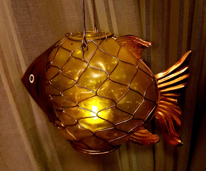 Upphängd fisk-formad lykta med ljus inuti som skapar en undervattenskänsla i rummet.