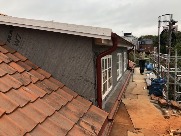 Renovering av hus med rött tak, vindskivor och fasadarbete pågår med arbetare och byggnadsställningar.