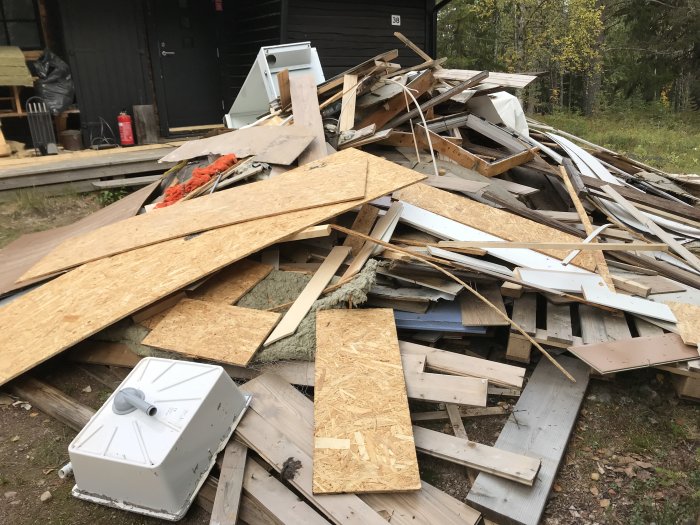 Hög med byggavfall bestående av träplankor, OSB-skivor och isoleringsmaterial.