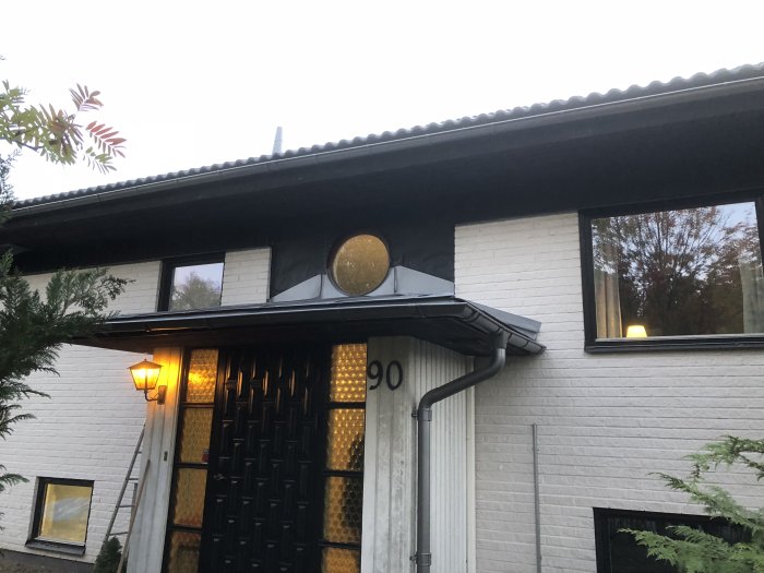 Husfasad med omonterad panel vid runt fönster och ny monterad panel vid altanen.