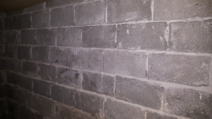 Fuktfläckar och vittring på en gammal källarmur av gråa betongblock, tecken på vatteninträngning.