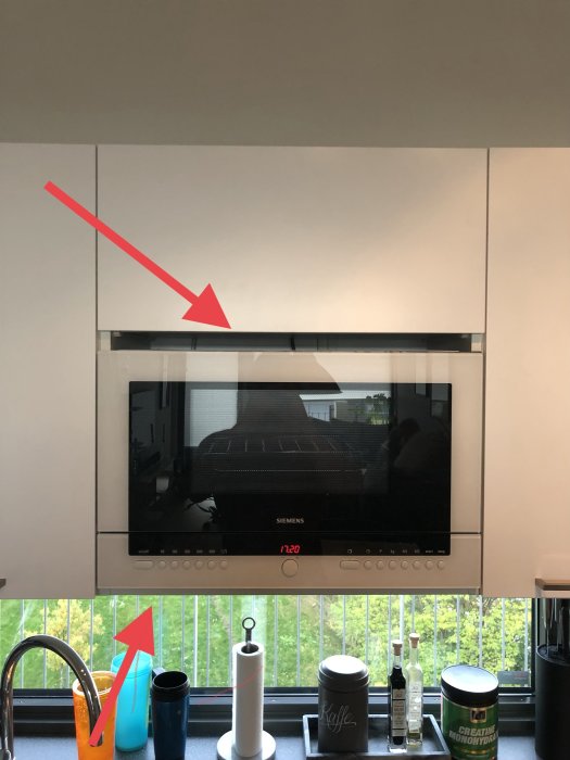 Kök med inbyggd mikrovågsugn, större glipa ovanför och mindre spalt nedanför, köksdetaljer på bänken.