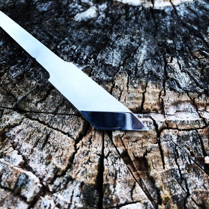 Handsmidd kniv med polerat blad på en grov trädstubbe.