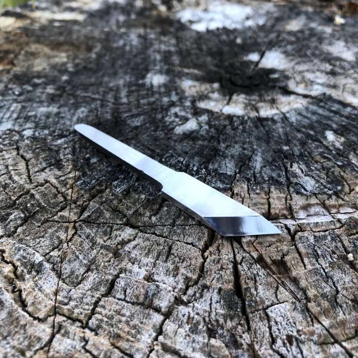 Handsmidd kniv med polerat blad som ligger på en trädstubbe med sprickor.