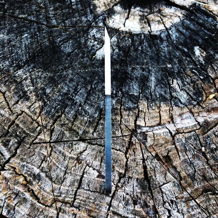 Handsmitt kniv av stål ligger centralt på åldrad trädstubbe.