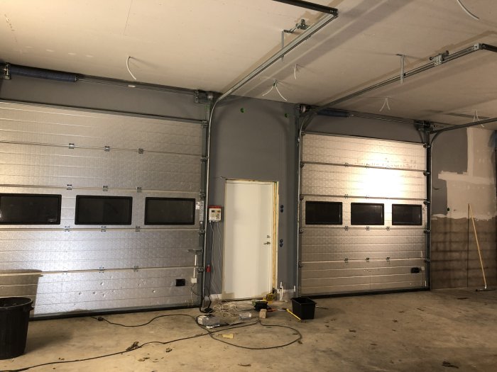 Insidan av en garagebyggnad med nyinstallation av en isolerad garageport och en sidodörr.