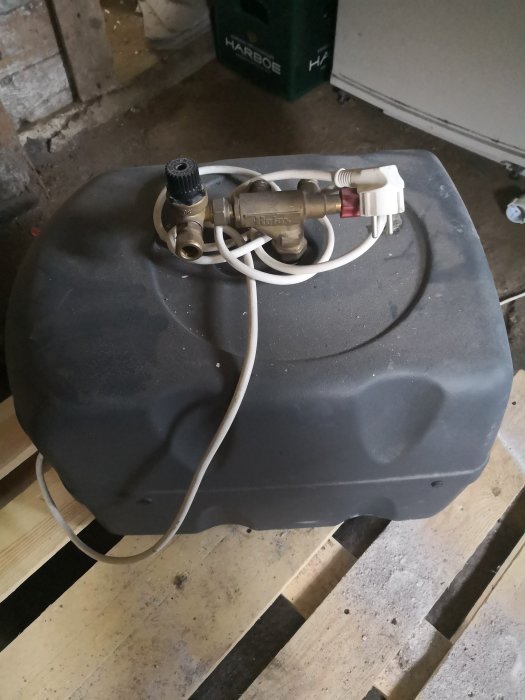 Begagnad portabel varmvattenberedare på golvet, kopplad med slangar och elkabel.