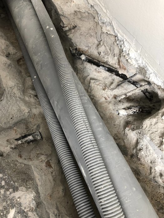 Pansarrör och ledningar som är uppbilade ur betonggolv och vägg, syns i rörigt tillstånd vid renovering.