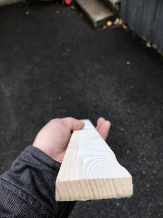 En hand håller en nyslipad och målad träbit formad som ett omvänt L.