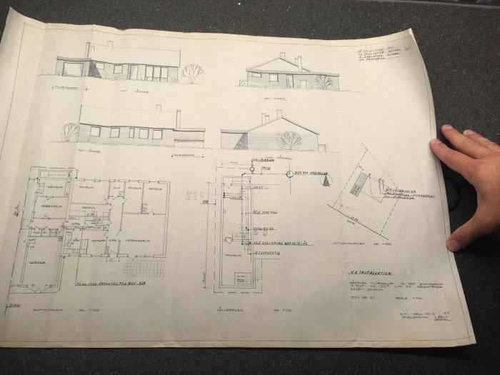 Hand som håller i en planritning av ett hus inkluderande väggstrukturer och rumsuppdelningar.