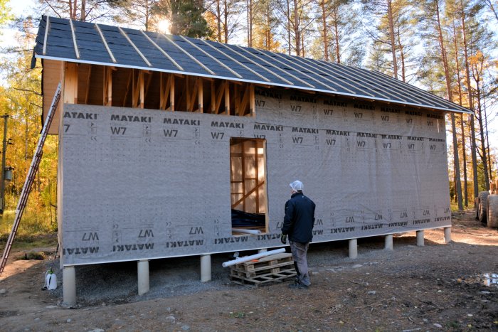 Hus under konstruktion klätt i vindväv med en person framför som betraktar arbetet.