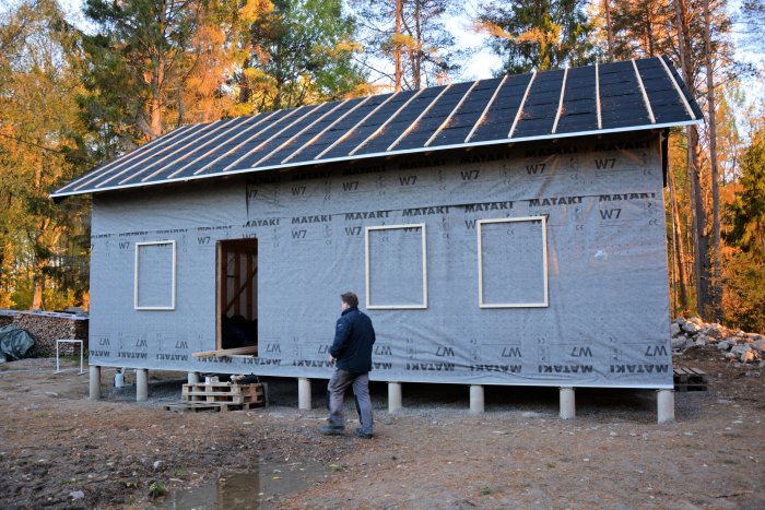 Hus under konstruktion klätt i vattentät vindväv med synliga 45-reglar runt fönster och dörrar.