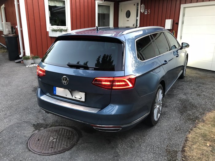 Blå Volkswagen Passat GTE kombi parkerad framför ett rött hus och en vit garageport.