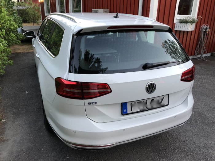 Vit Volkswagen Passat GTE parkerad framför en röd byggnad med laddstation till vänster.