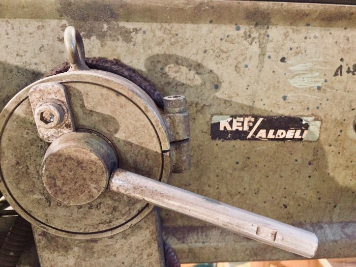 Närbild på en rostig del av en dieselpunk-maskin med en vev och märkesetiketten "KEF/Aldel".