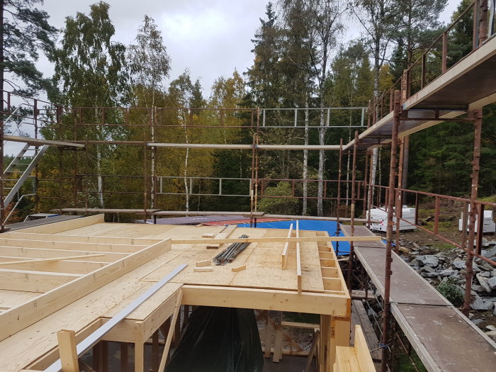 Ställning vid bygge av andra våningen på ett hus, omgiven av träd.