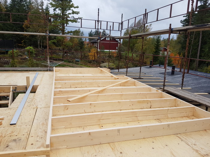 Monterad byggnadsställning och påbörjade träbjälklag för andra våningen på ett husbygge.