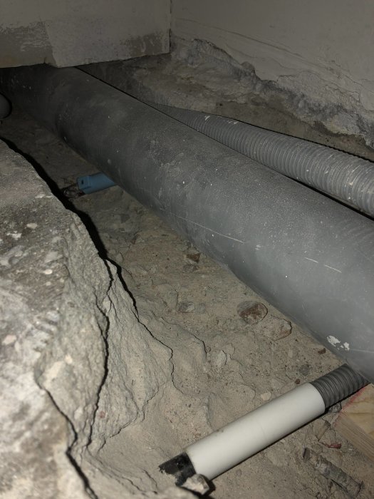 Elektriska installationer med pansarrör och kablar som går genom betonggolv i ett badrumprojekt.