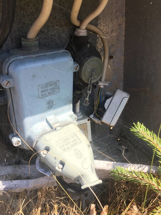 Öppet elskåp med lösa kablar och kontakter nära en strand, risk för barn som leker i närheten.