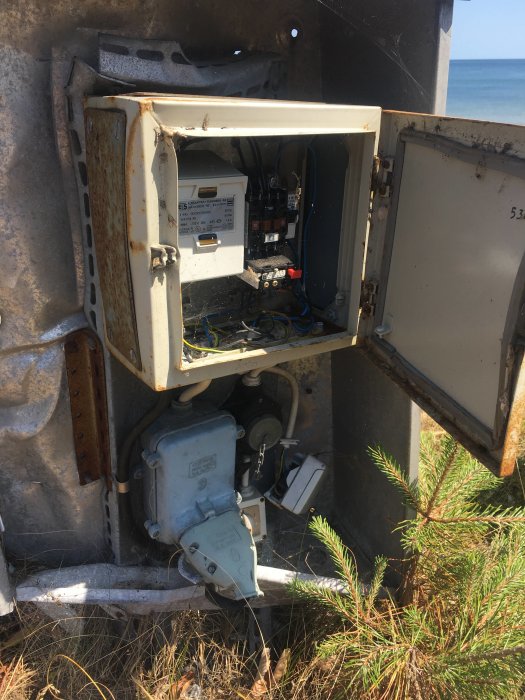 Öppet elskåp med sladdar och säkringsutrustning, utan avgränsning, nära en strand.