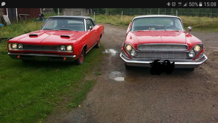 Dodge Coronet -69 cabriolet i rött till vänster och röd Desoto -61 4dr ht till höger parkerade utomhus.
