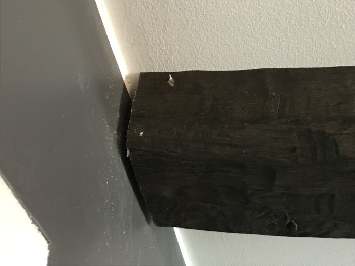 Brunsvart plastbjälke som inte helt möter en vitmålad vägg, med synligt mellanrum i behov av spackling.