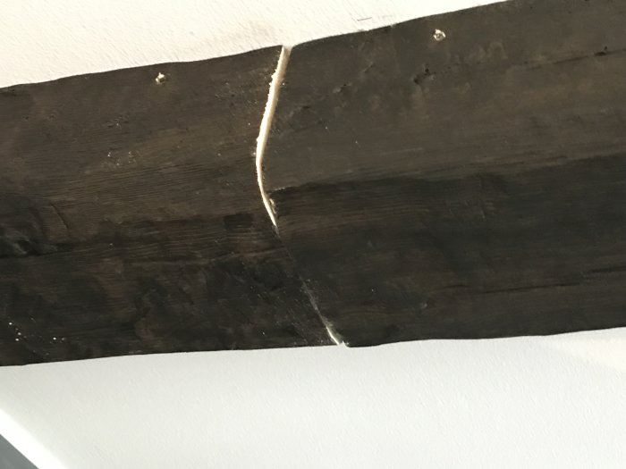 Brunsvart plastbjälke monterad i taket med synligt mellanrum till en vit vägg.